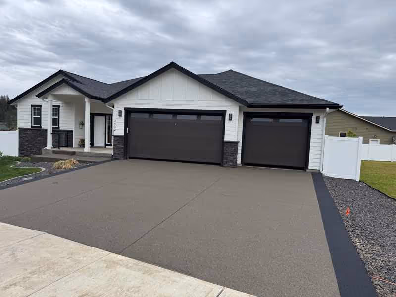Wide new concrete driveway leading to a modern two-garage home