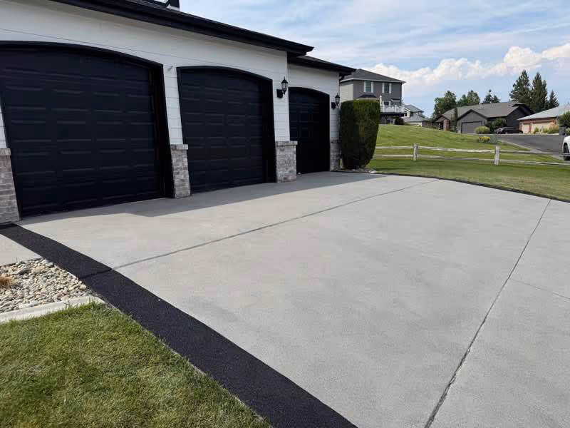 Resurfaced two-car concrete driveway in front of black garage doors
